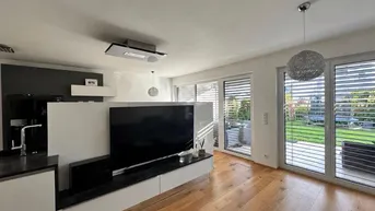 Helles Wohnzimmer mit Holzboden, großem Fernseher und direktem Zugang zum Gartenbereich.