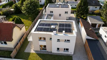 Luftaufnahme von zwei modernen Häusern mit Flachdächern und Photovoltaikanlagen in einer Wohnsiedlung.