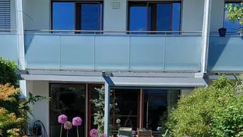 Moderne Reihenhausfassade mit gepflegtem Garten, Terrasse und Balkon im Obergeschoss.