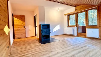 Geräumiges Wohnzimmer mit Holzwänden, Holzbalkendecke und einem gemütlichen Kaminofen.