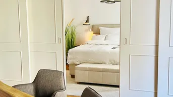 Blick durch die eleganten Schiebetüren in ein helles Schlafzimmer mit Parkettboden.