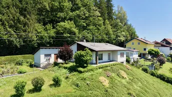 Freistehendes Einfamilienhaus auf einem Hügel mit viel Grünfläche und Wald im Hintergrund.