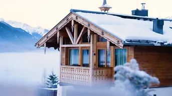 Nahaufnahme eines verschneiten Holzchalets mit traditionellen Verzierungen und Bergblick.