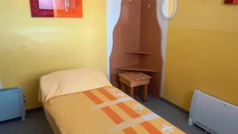 Gelb gestrichener Raum mit einer Behandlungsliege, Wandkunst und einem kleinen Beistelltisch.