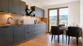 Moderne Küche mit dunklen Schränken, Holzakzenten und Essbereich mit Blick auf die grüne Landschaft.