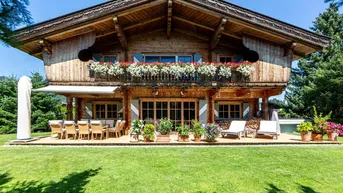 Großzügige Holzterrasse mit Essbereich und Liegestühlen vor einem traditionellen Chalet mit Blumenkästen.