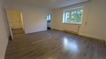 Helles Wohnzimmer mit modernem Laminatboden und Blick ins Grüne durch das Fenster.