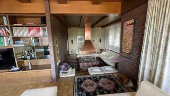 Wohnzimmer mit einem markanten Kamin, Ziegelwänden, Holzdecke und Parkettboden.
