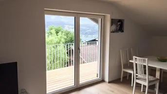 Heller Wohn- und Essbereich mit Holzboden, Dachschrägen und Zugang zu einem Balkon mit Seeblick.