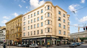Historisches Eckgebäude in städtischer Umgebung mit Geschäften im Erdgeschoss und vielen Fenstern.