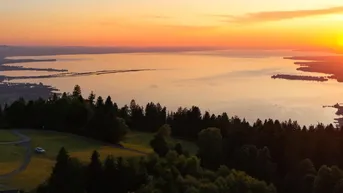 Atemberaubender Sonnenuntergang über einem weiten See, umgeben von bewaldeten Hügeln und einer weiten Landschaft.