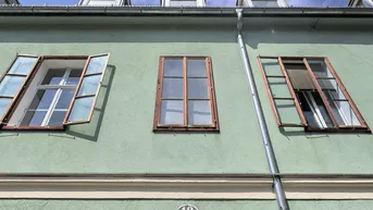 Fassade eines Altbaus mit mehreren Fenstern und Dachgauben unter blauem Himmel.