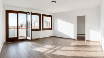Helles, leeres Wohnzimmer mit großen Fenstern, Laminatboden und Zugang zu einem Balkon.