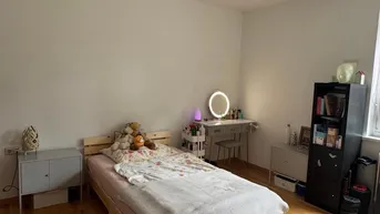 Helles Schlafzimmer mit Holzbett, Schreibtisch und einem runden Teppich auf Parkettboden.