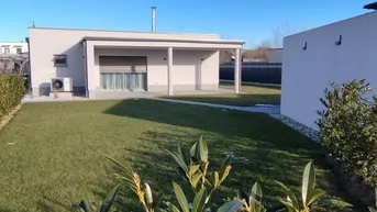 Modernes Einfamilienhaus mit gepflegtem Rasen, überdachter Terrasse und leichter Schneedecke.