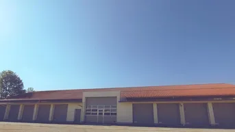 Langes Gebäude mit mehreren Garagentoren und einem großen Eingang unter klarem blauem Himmel.