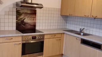 Funktionale Küche mit hellen Holzfronten, Einbaugeräten und Fliesenboden im Arbeitsbereich.