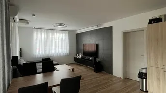 Geräumiger Wohn- und Essbereich mit modernem Holzboden, dunkler Akzentwand und viel Tageslicht.