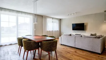 Heller Wohn- und Essbereich mit Holzboden, großen Fenstern und modernem Sofa.