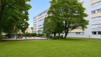 Große Grünfläche mit Spielplatz und Bäumen vor einem Mehrfamilienhaus.
