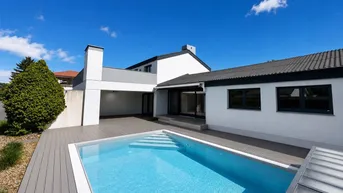 Modernes Haus mit privatem Swimmingpool und Holzterrasse unter blauem Himmel.