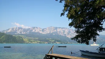Idyllischer Seeblick mit Bergen im Hintergrund und kleinem Holzsteg am Ufer.