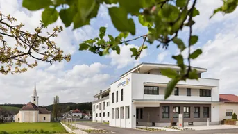 Modernes Gebäude mit klarer Architektur und Blick auf eine Kirche im Grünen.