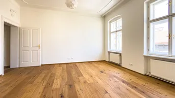 Helles Zimmer mit elegantem Parkettboden, hohen Decken und Stuckverzierungen, ideal für Wohn- oder Schlafbereich.