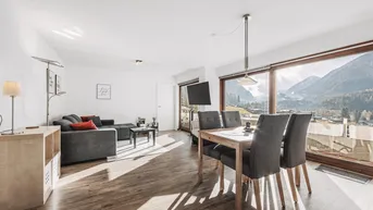 Helles Wohn- und Esszimmer mit Holzboden, gemütlicher Sitzecke und beeindruckendem Bergblick.