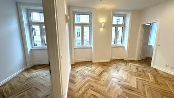 Helles Zimmer mit Fischgrätparkett und mehreren Fenstern, ideal als Wohnzimmer nutzbar.