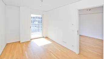 Helles Zimmer mit Holzboden und Zugang zu einem Balkon, ideal als Wohn- oder Schlafbereich.