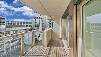 Geräumiger Balkon mit Holzboden und Glasgeländer, bietet einen Blick auf die umliegenden Gebäude.