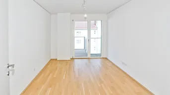 Helles, leeres Zimmer mit Parkettboden und Zugang zu einem Balkon in einem Neubau.