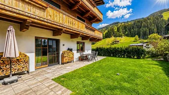 Sonnige Terrasse mit Garten, Bergblick und traditioneller Holzfassade eines Chalets in alpiner Umgebung.