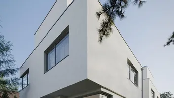 Moderne weiße Stadtvilla mit großen Fenstern und einer kleinen Terrasse im Grünen.
