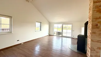 Helles Wohnzimmer mit Holzboden, Dachschrägen und einem modernen Kaminofen.