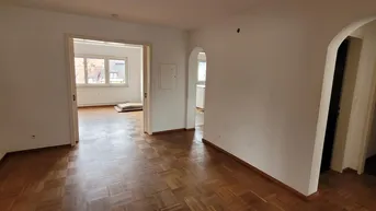 Geräumiges Wohnzimmer mit Parkettboden und mehreren Zugängen zu anderen Räumen.