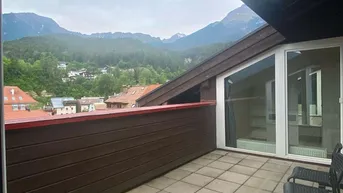 Große Terrasse mit Fliesenboden, Holzelementen und einem weiten Blick auf die Berge.