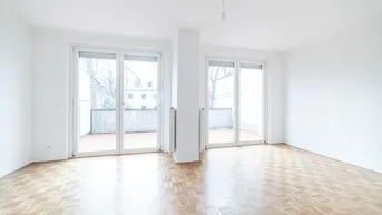 Helles Wohnzimmer mit Parkettboden und zwei Zugängen zu einem Balkon.