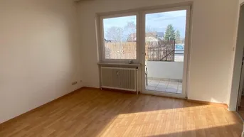 Helles Wohnzimmer mit Laminatboden und Zugang zu einem kleinen Balkon, gut beleuchtet durch Tageslicht.
