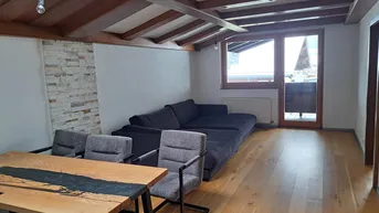 Geräumiger Wohn- und Essbereich mit Holzbalkendecke, Parkettboden und Zugang zum Balkon.