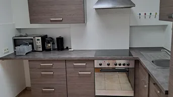 Funktionale Küche mit Holzoptik-Schränken, Fliesenboden und integrierten Geräten.