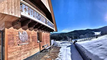 Winterliches Holzchalet mit weitem Blick auf die verschneite Landschaft und Skipisten.