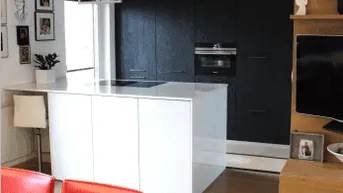 Moderne offene Küche mit weißer Insel, schwarzen Einbauschränken und hellem Holzfußboden.