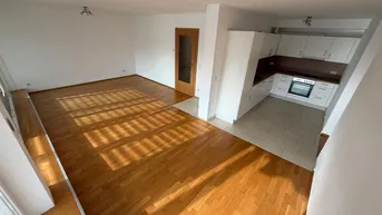 Heller Wohn- und Essbereich mit Parkettboden und integrierter Küchenzeile, durchflutet von natürlichem Licht.