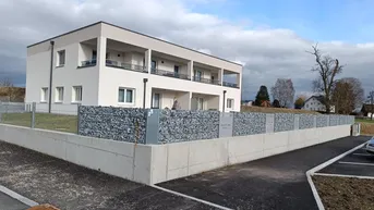 Modernes Mehrfamilienhaus mit heller Fassade, Balkonen und Gabionenmauer im Außenbereich.