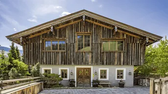 Traditionelles Holzchalet mit Steinfassade und gepflastertem Eingangsbereich unter blauem Himmel.