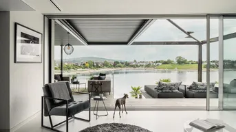 Modernes Wohnzimmer mit großen Schiebetüren, die sich zu einer Terrasse mit Seeblick öffnen.