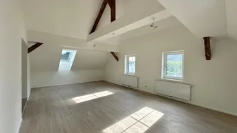 Geräumiger Dachgeschossraum mit sichtbaren Holzbalken, Dachfenster und hellem Laminatboden.