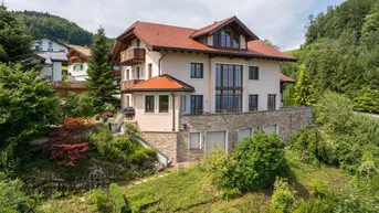 Großzügiges Einfamilienhaus mit mehreren Balkonen und Terrassen in Hanglage, umgeben von viel Grün.